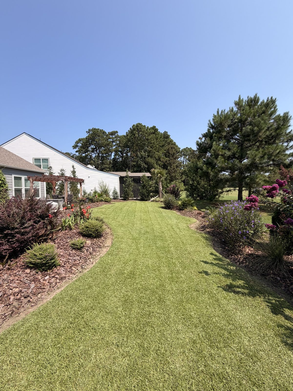 Curved lawn path lined with colorful garden beds and a pergola