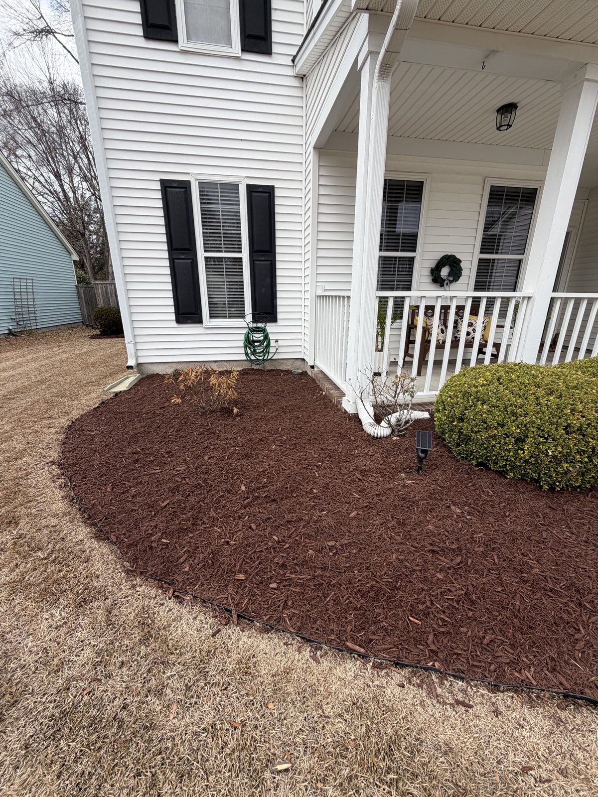 Fresh brown mulch installation in a front bed beside a white porch