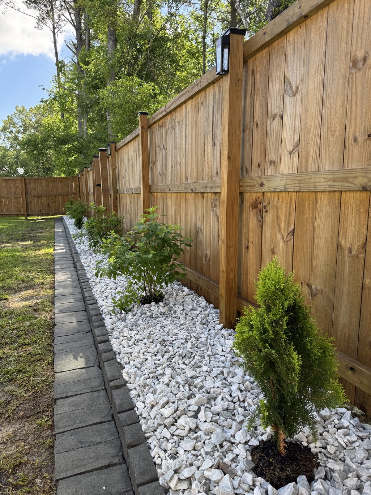 Redesigned fence-line bed with white rock, new shrubs, and paver edging