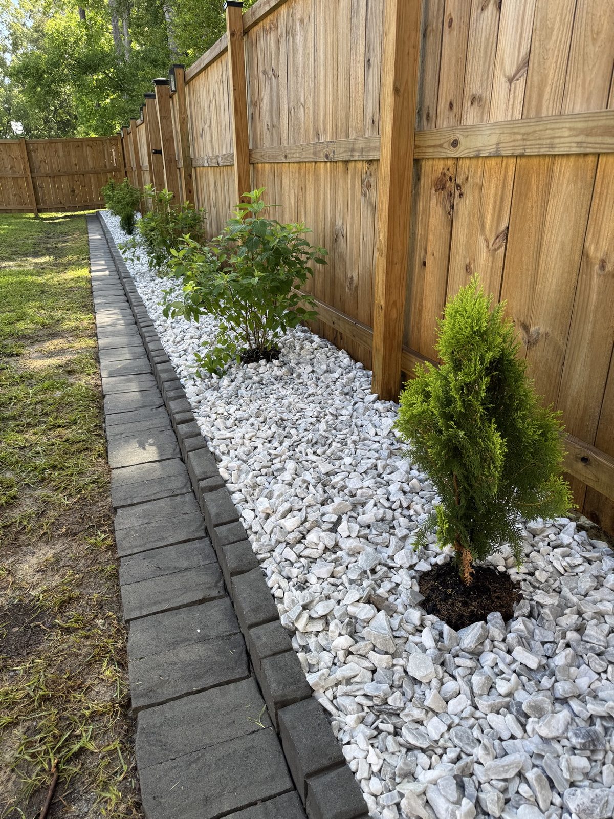 Bed redesign with white marble rock and fresh plantings along a wooden fence
