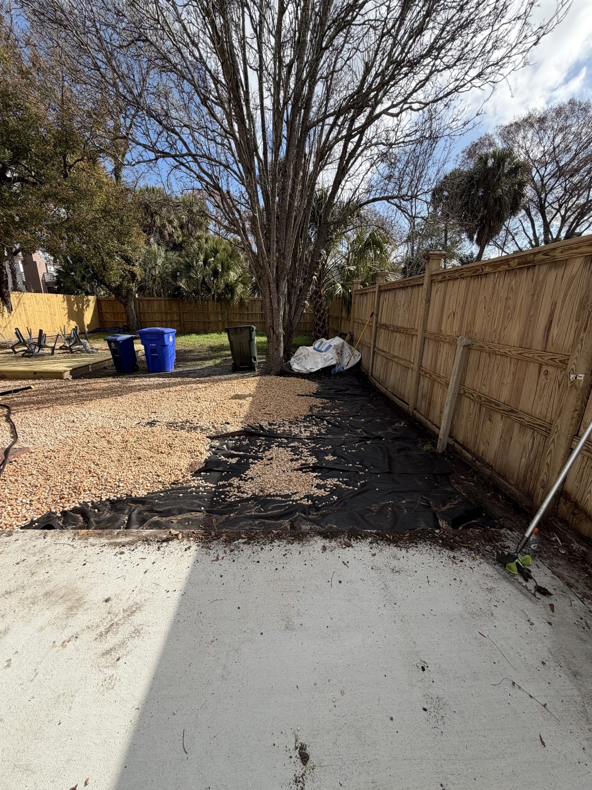 Rock installation in progress over landscape fabric along a fence